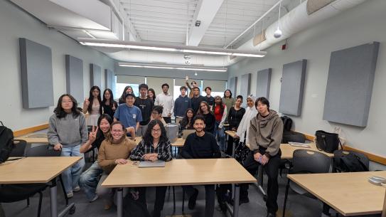 Large group of students posed in a classroom with professor Bertha Jimenez