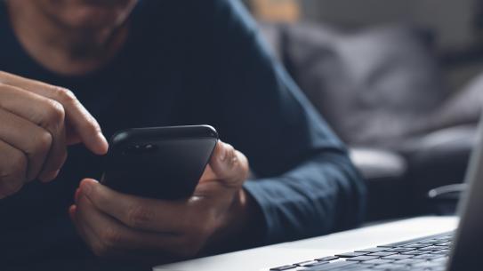 close up of person holding a mobile by an open laptop