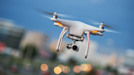 A drone in flight, with a camera attached to the bottom.