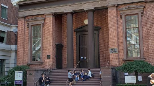 students sitting on steps of brick building with columns
