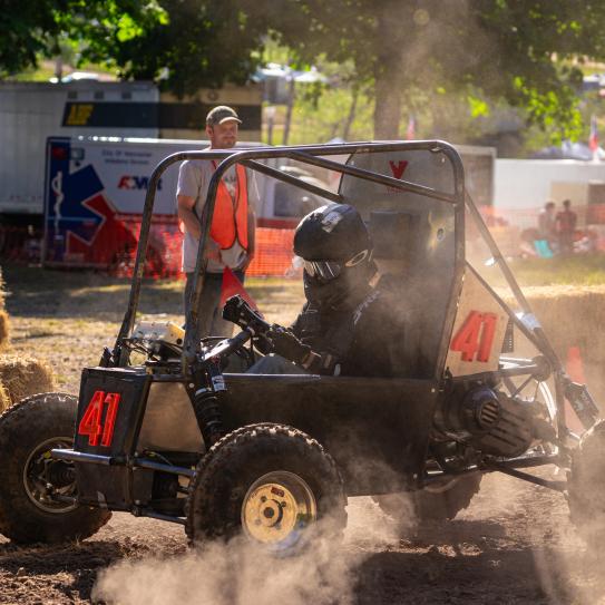 Picture of Baja SAE riding on the dirt road and a few people looking